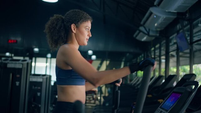 Young sportswoman exercising on elliptical cardio machine in fitness gym.