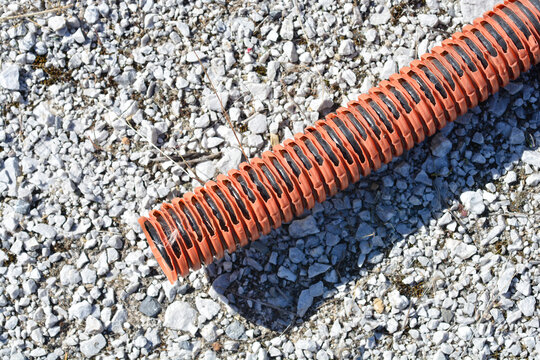 Close up detail of a broken and cracked orange corrugated plastic conduit pipe laying abandoned on a rough gravel surface at a construction site.
