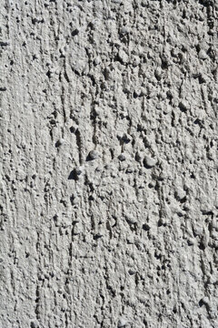 ull frame background texture of a rough and bumpy grey stucco plaster surface with vertical scratch marks and pebble textures.