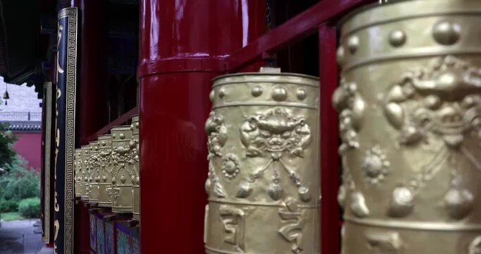 Golden Tibetan prayer wheels with intricate lion and mantra carvings beside red temple pillars in a traditional Buddhist monastery