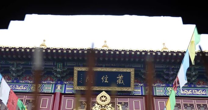 Golden Tibetan prayer wheel and ornate 'Zang Jing' signboard on traditional temple facade with colorful prayer flags