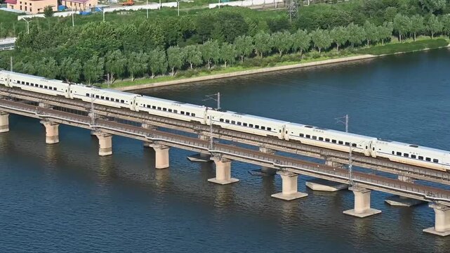 High-speed train crossing a multi-track bridge over a wide river under bright daylight