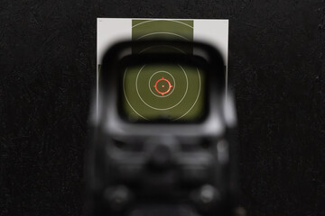 First person point of view looking through holographic optic red reticle aiming at center of paper target in shooting range © Dmitri