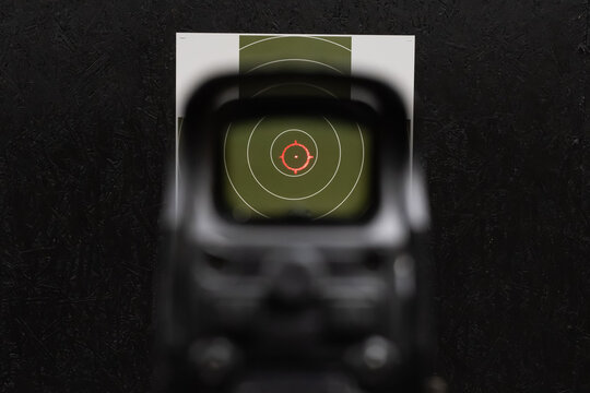 First person point of view looking through holographic optic red reticle aiming at center of paper target in shooting range
