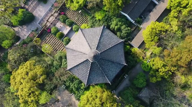 Aerial drone footage of a traditional Chinese octagonal pavilion with gray tiled roof nestled among vibrant green trees, transitioning to a towering multi-tiered pagoda beside a serene lake