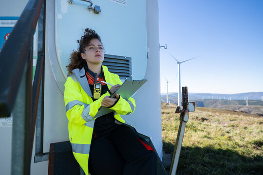 White woman technician inspecting wind turbine at wind farm in Galicia