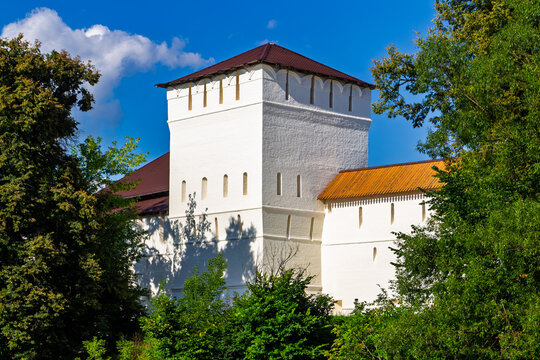 Ancient white stone fortification tower of St. Pafnutius Borovsky Monastery surrounded by lush green trees under a bright blue summer sky in Borovsk, Russia