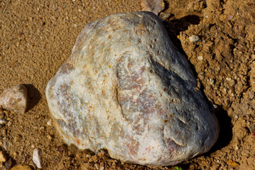 Massive quartz boulder rests in quarry dirt, showing rugged geological texture and natural mineral patterns under bright daylight © PhotoChur