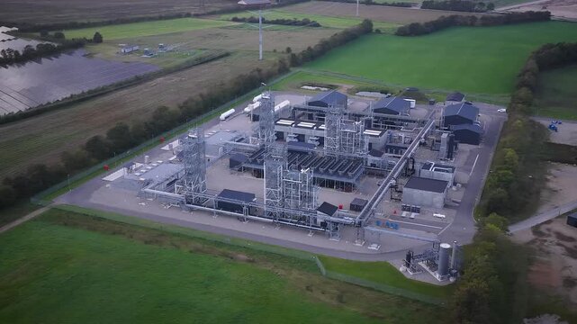 Aerial orbit of E-methanol power-to-x plant in Denmark. State-of-the-art Power-to-X facility by green fields and vast solar park showcasing integration of renewable energy and green fuel production.