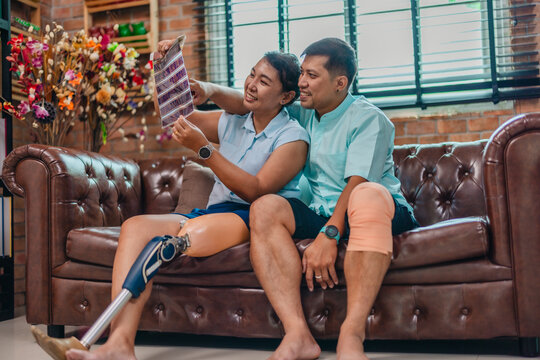 Wife with prosthetic leg and husband reminiscing over old film negatives on sofa, side view
