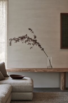 Gray sofa, wooden console, dried branch in ceramic bowl, neutral beige tones, zen aesthetic, serene home, wabi-sabi design, contemporary lifestyle, mindful living.