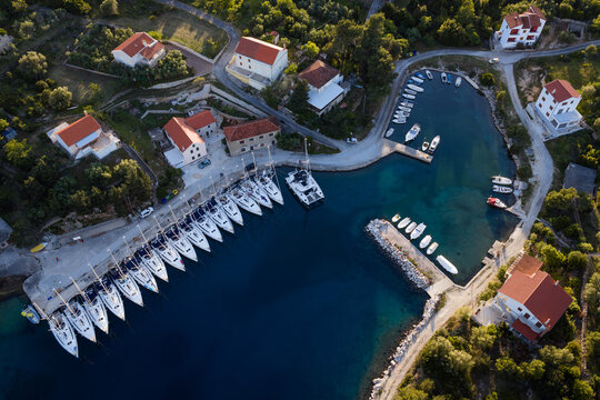Aerial top view of small coastal harbor with line of sailboats and traditional houses at sunset