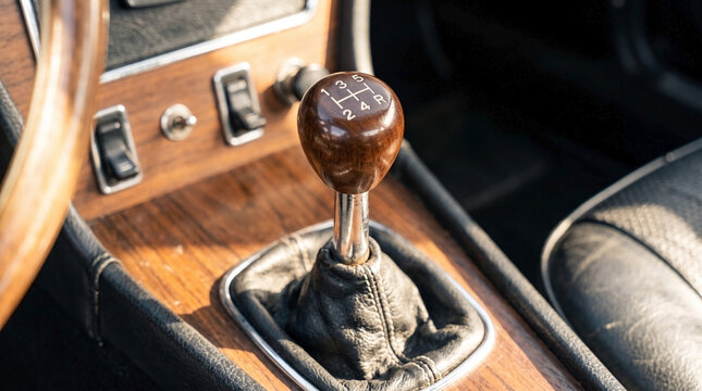 Retro car gear shift knob with wooden handle and leather boot in vintage car interior. Nostalgic design features chrome accents and detailed engravings, enhancing classic automotive appeal.