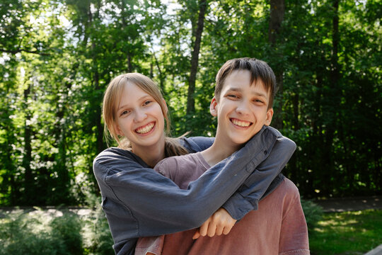 Smiling teenage girl hugs her brother outdoors in a summer park