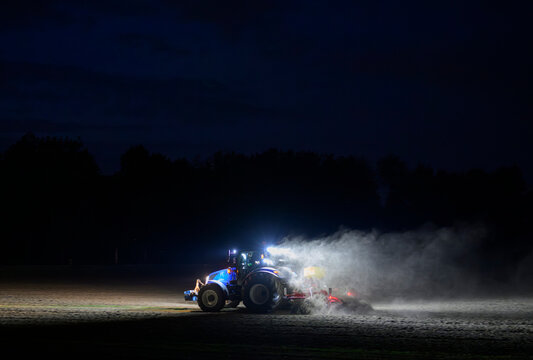 A tractor sows a dry dusty field at night in Flevoland