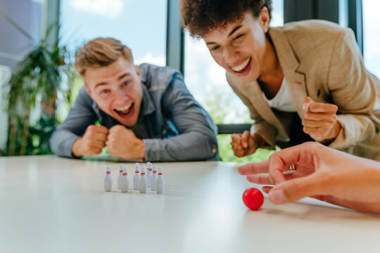 A man and woman play miniature bowling on an office desk