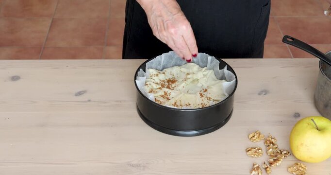 Female Hands Sprinkling Brown Sugar over Apple Pie with Puff Pastry Crust. Female hands sprinkle brown sugar over the surface of a puff pastry apple pie before baking.