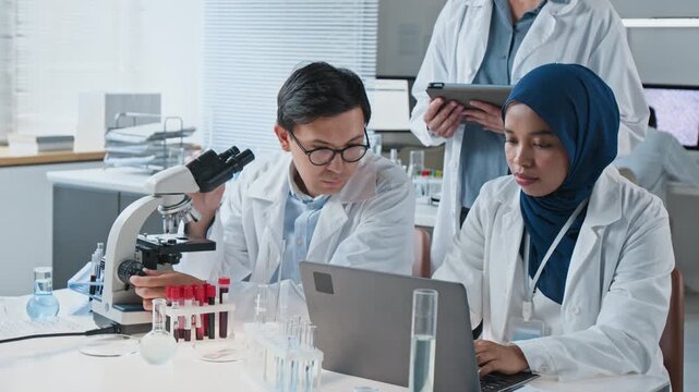 Diverse young adult scientists analyzing medical samples using microscope and laptop in laboratory. Footage suitable for pharmaceutical research, medical education and biotechnology marketing
