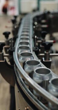 Empty aluminum cans move along curved conveyor inside automated brewery plant. Precision guide rails maintain alignment supporting continuous factory transport