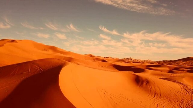 Aerial Drone view of sweeping orange sand dunes with wind sculpted ridges beneath a warm sunset sky. Vast desert terrain stretches toward the distant horizon in Mauritania.