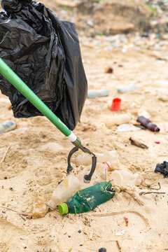Volunteer using trash picker to collect plastic bottles on a polluted beach