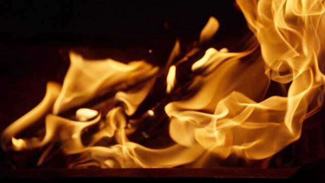 Close-up shot of bright yellow and orange fire flames dancing and burning brightly against a dark night background