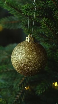 Vertical video. Woman decorating Christmas tree with golden Christmas ball.