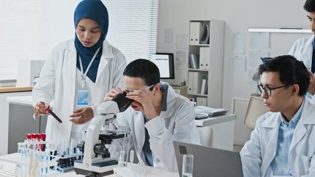 Diverse multiethnic team of young adult scientists conducting medical research with microscope and test tubes in laboratory. Footage ideal for biotechnology or pharmaceutical marketing