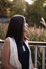 Side view profile portrait of young dark-haired woman in white sleeveless vest looking away outdoors at sunset © Alya