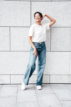 Young beautiful smiling hipster woman in trendy summer white t-shirt and jeans clothes. Carefree woman, posing in the street at sunny day. Positive model outdoors near wall. Going crazy