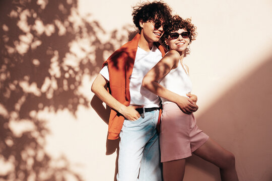 Young smiling beautiful woman and her handsome boyfriend in casual summer clothes. Happy cheerful family. Female having fun. Couple posing in street at sunny day. Near wall at sunset. In sunglasses