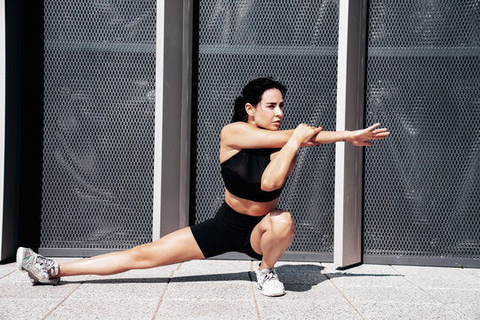Fitness woman in sports clothing. Sexy young beautiful model athlete doing fitness workout. Female making exercises in the street at sunny day. Stretching out before training. Posing near urban wall