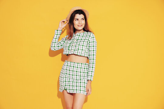 Young beautiful smiling female in trendy summer green costume clothes. Carefree woman posing near yellow wall in studio. Positive model having fun indoors. Cheerful and happy. Jacket and skirt, hat