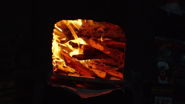Firewood slowly burning and forming hot glowing embers inside a dark fireplace, creating a warm, cozy, and relaxing atmosphere