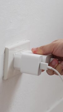 close up hand plugging adapter charge the battery with outlet socket plug and hold mobile phone on wall ,electric safety concept