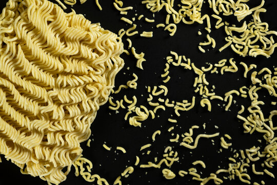 Raw instant ramen noodle block with scattered small noodle bits on black background
