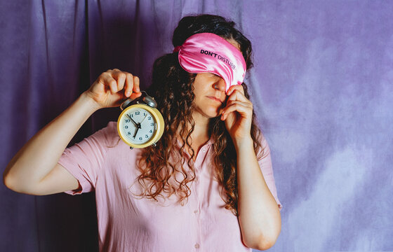 Tired woman in pajamas holds an alarm clock