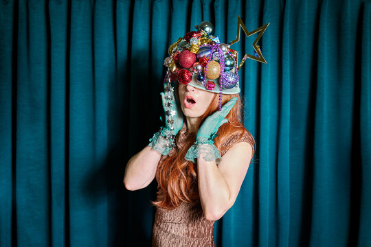 A festive woman wears a whimsical hat made of christmas ornaments