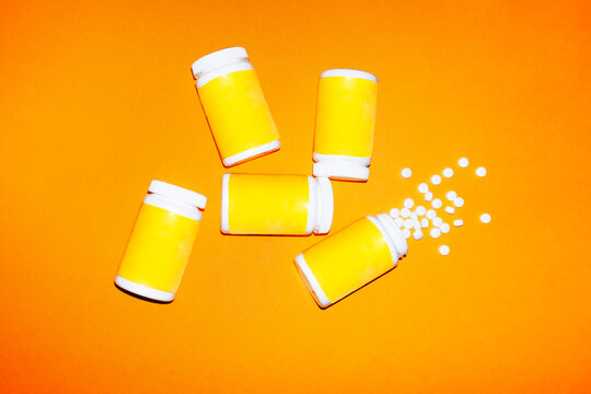 White vitamin pills spilling from yellow bottle on orange background