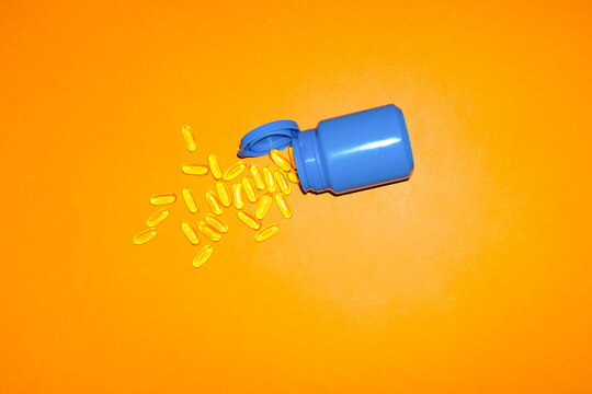 A blue bottle spills yellow vitamin pills on an orange background