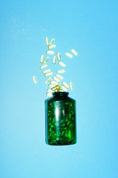 Green bottle spilling dietary supplement on blue background