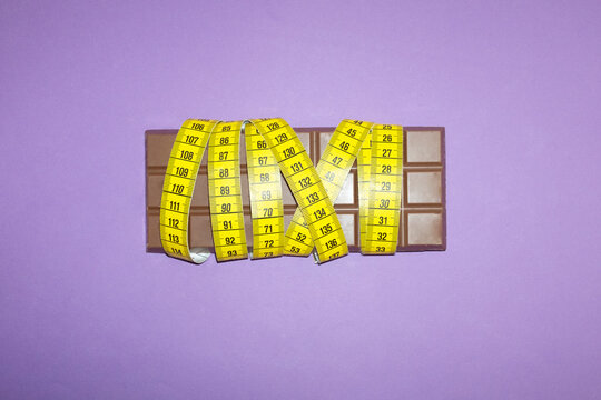 A yellow tape measure wraps around a chocolate bar