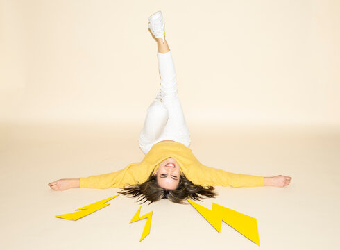 Woman in yellow sweater on floor with paper lightning bolts and energetic pose