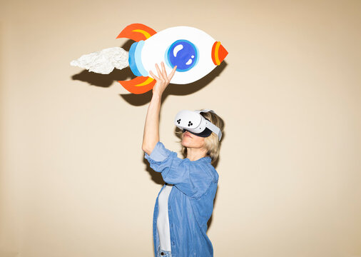 Woman wearing virtual reality headset holds paper rocket