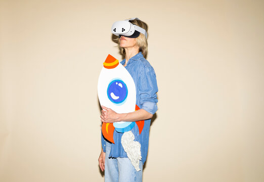 Woman wearing virtual reality headset holds paper rocket indoors