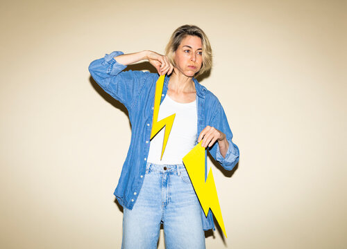 Stressed woman holds a broken paper lightning bolt indoors