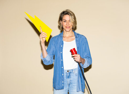 Smiling woman holds lightning bolt and charging cable indoors