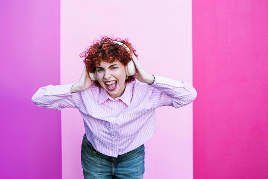 Enthusiastic redhead singing with headphones on pink background