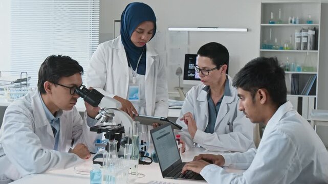 Diverse group of young adult scientists conducting research using microscope, laptop, and digital tablet in laboratory. Ideal for medical research or biotechnology corporate videos