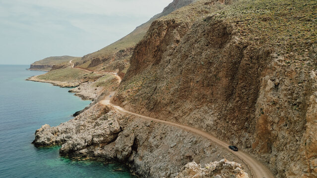 Drone view of narrow unpaved dirt road carved into steep rocky cliff along sea coast on route to Balos lagoon in Gramvousa Crete Greece